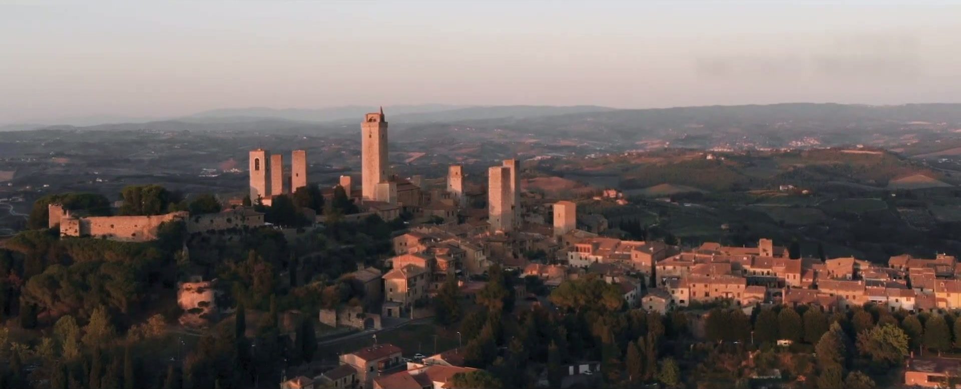 Panoramic view of San Gimignano's stone towers and rooftops above the Tuscan countryside at sunset