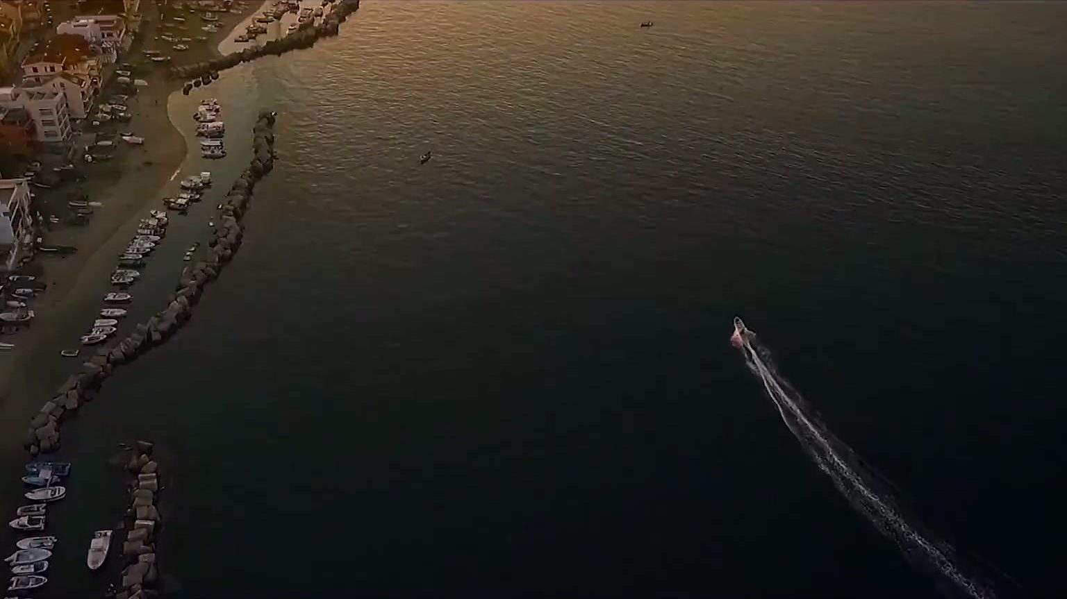 A boat crossing calm water beside a Sicilian coastal village in warm evening light