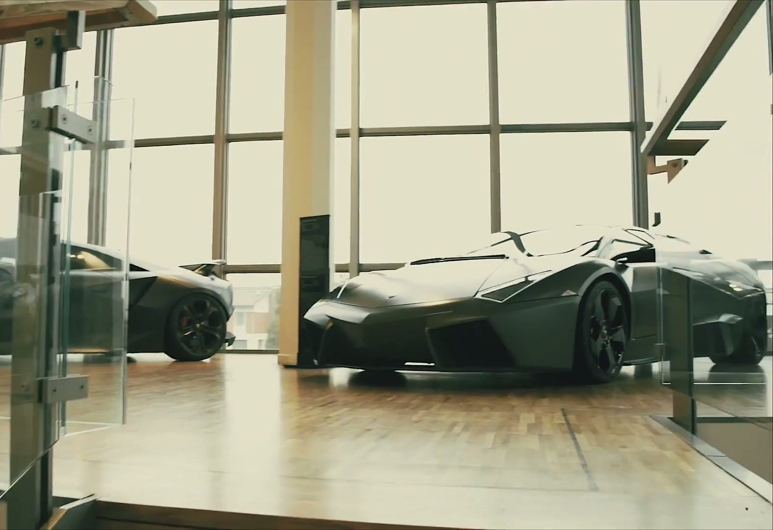 A dark Lamborghini supercar displayed in a sunlit museum gallery