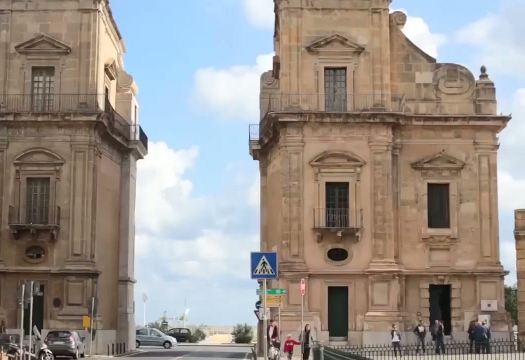 Ornate Sicilian Baroque church facades framing a street beneath a blue sky
