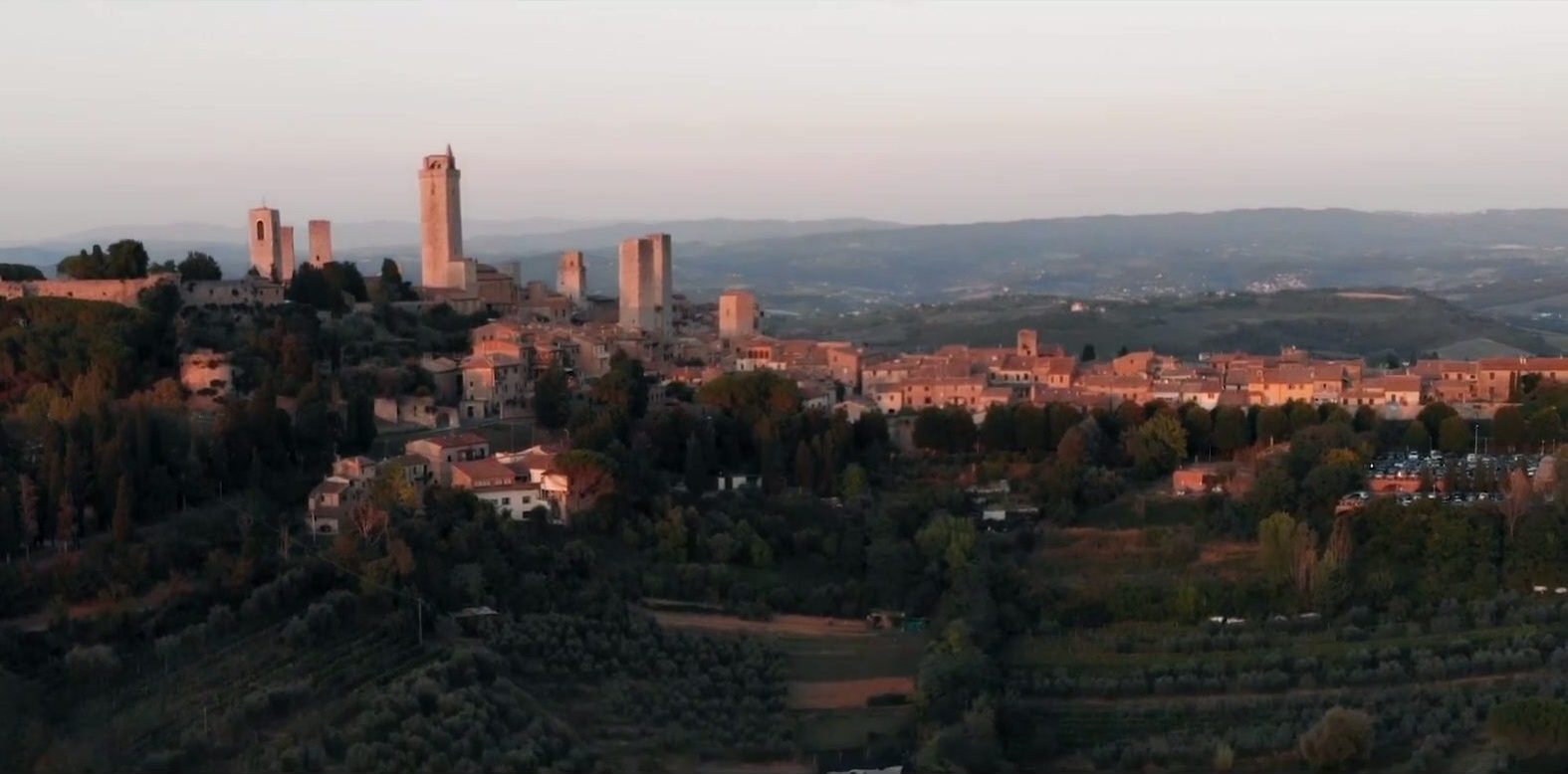 San Gimignano's medieval towers above wooded Tuscan hills in warm evening light