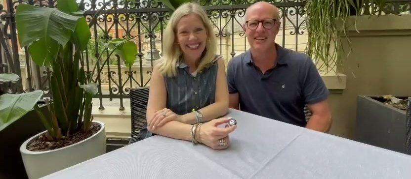 Una pareja de clientes sonriente sentada a una mesa en una terraza con vegetación