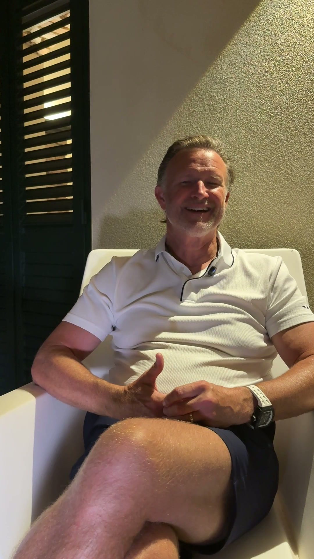 A smiling client seated on a sunlit terrace in a white polo shirt