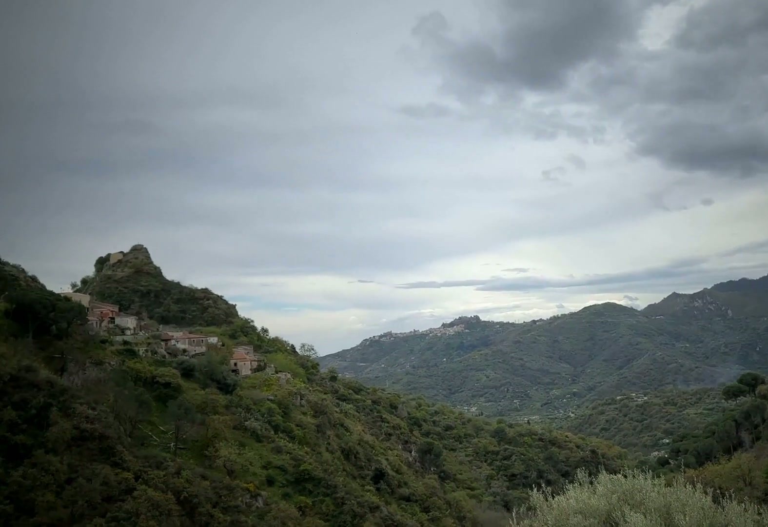 Savoca's hilltop ruins above a green Sicilian valley beneath a dramatic cloudy sky
