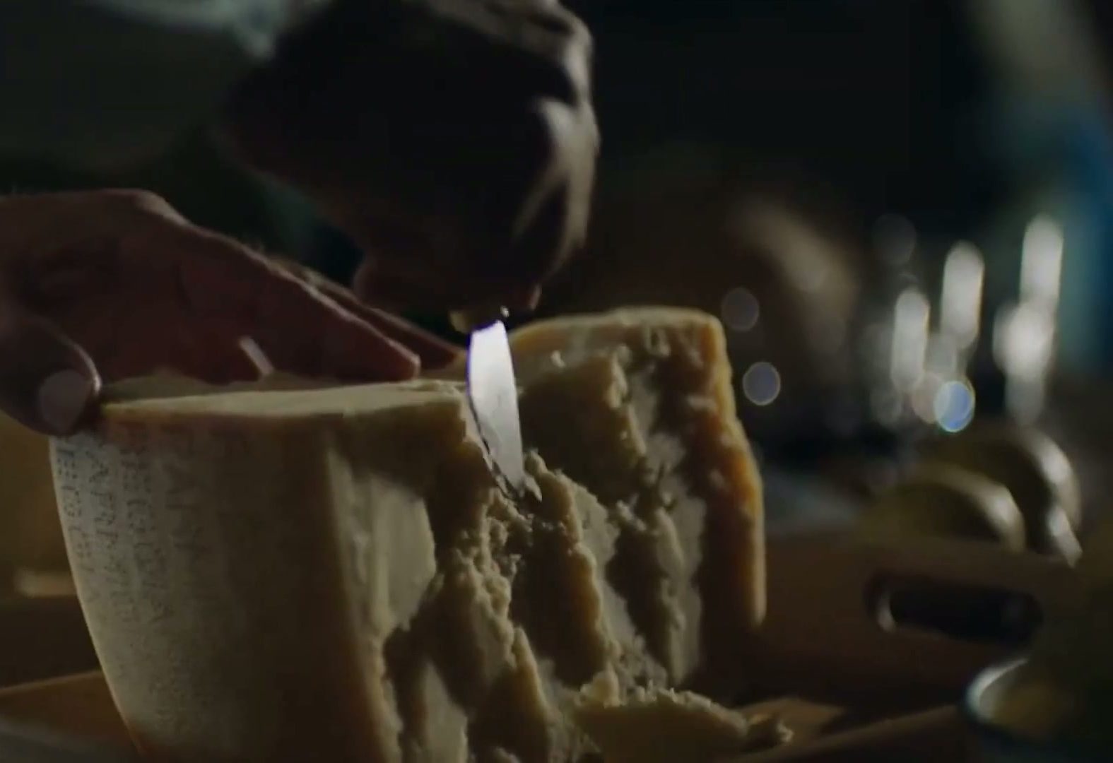 Hands cutting a wheel of Parmigiano Reggiano for a tasting