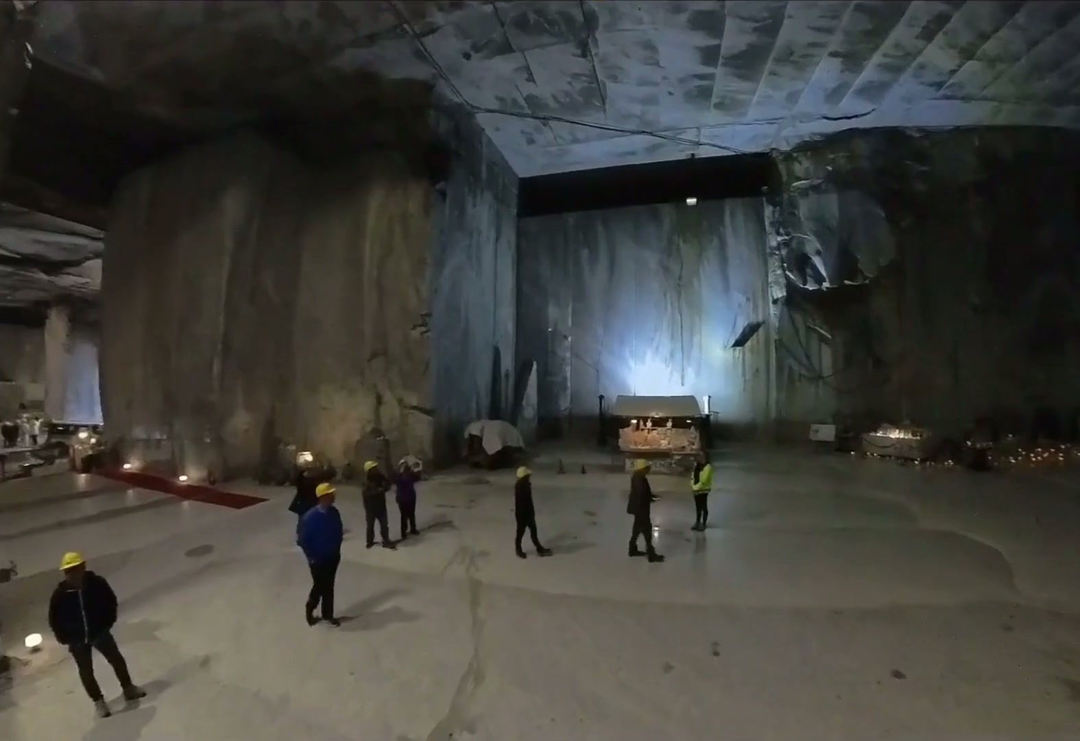Visitors in hard hats inside a vast Carrara marble quarry chamber