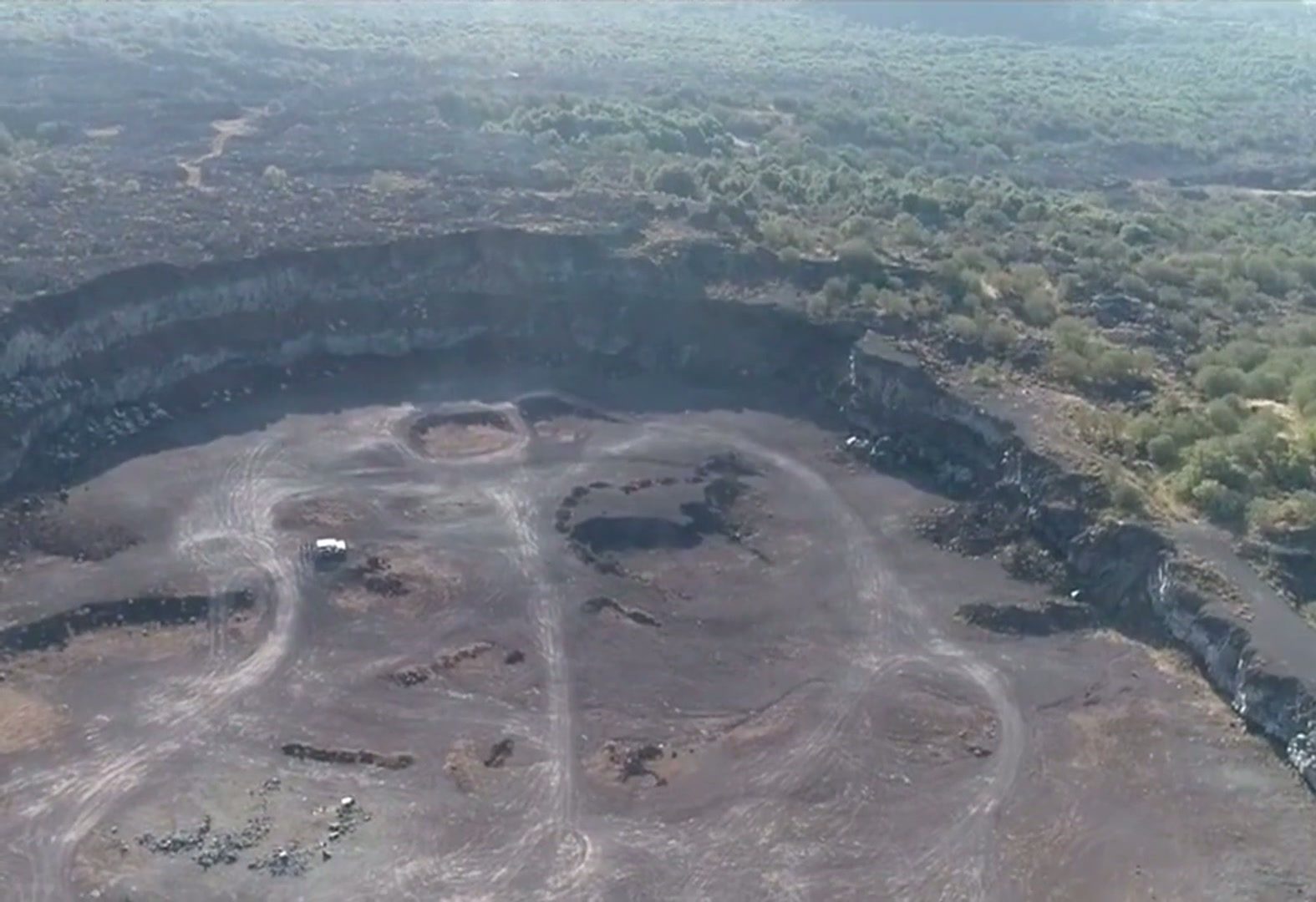 Aerial view of Etna's volcanic craters bordered by green woodland