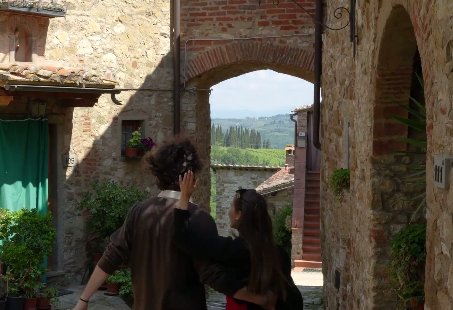 Couple strolling under a stone archway in a Chianti village, vineyards beyond