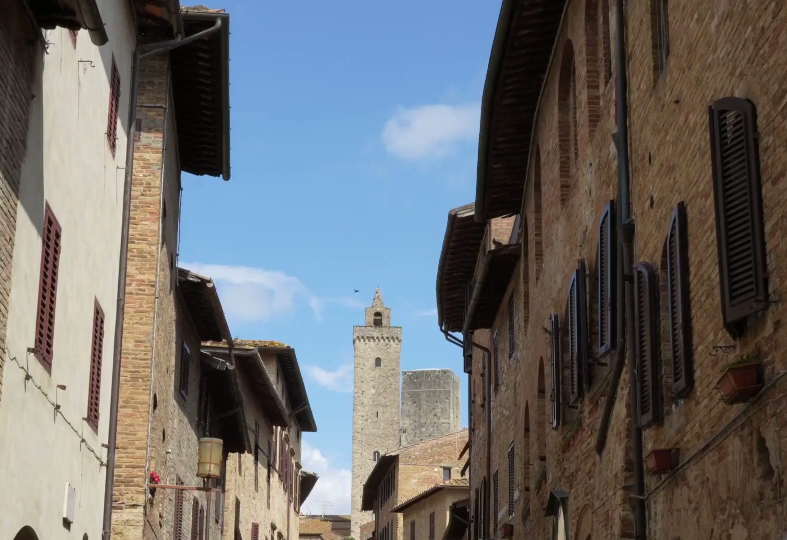 Medieval street in San Gimignano with a stone tower against blue sky