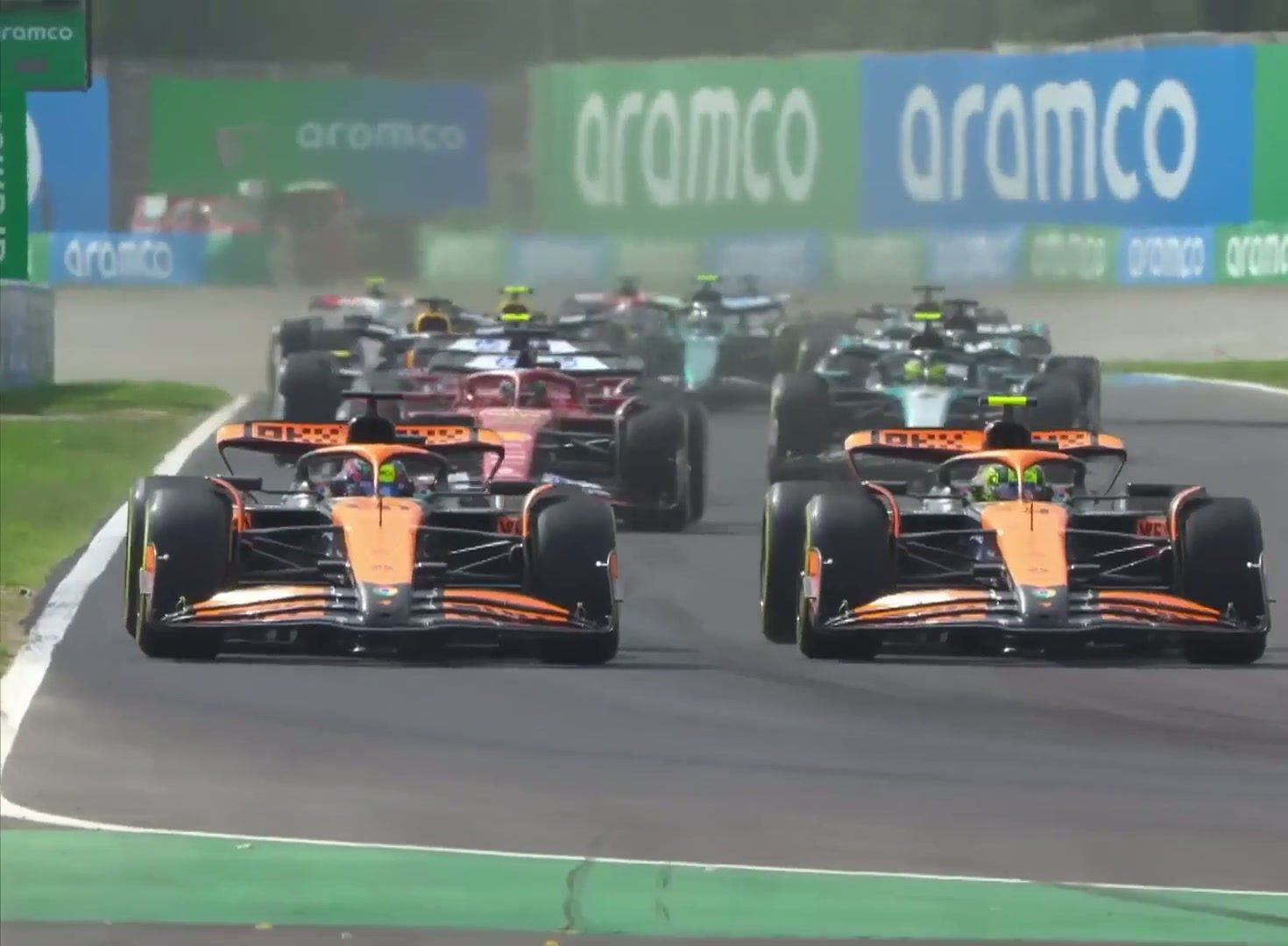 Two orange Formula 1 cars leading a pack of racers on the circuit