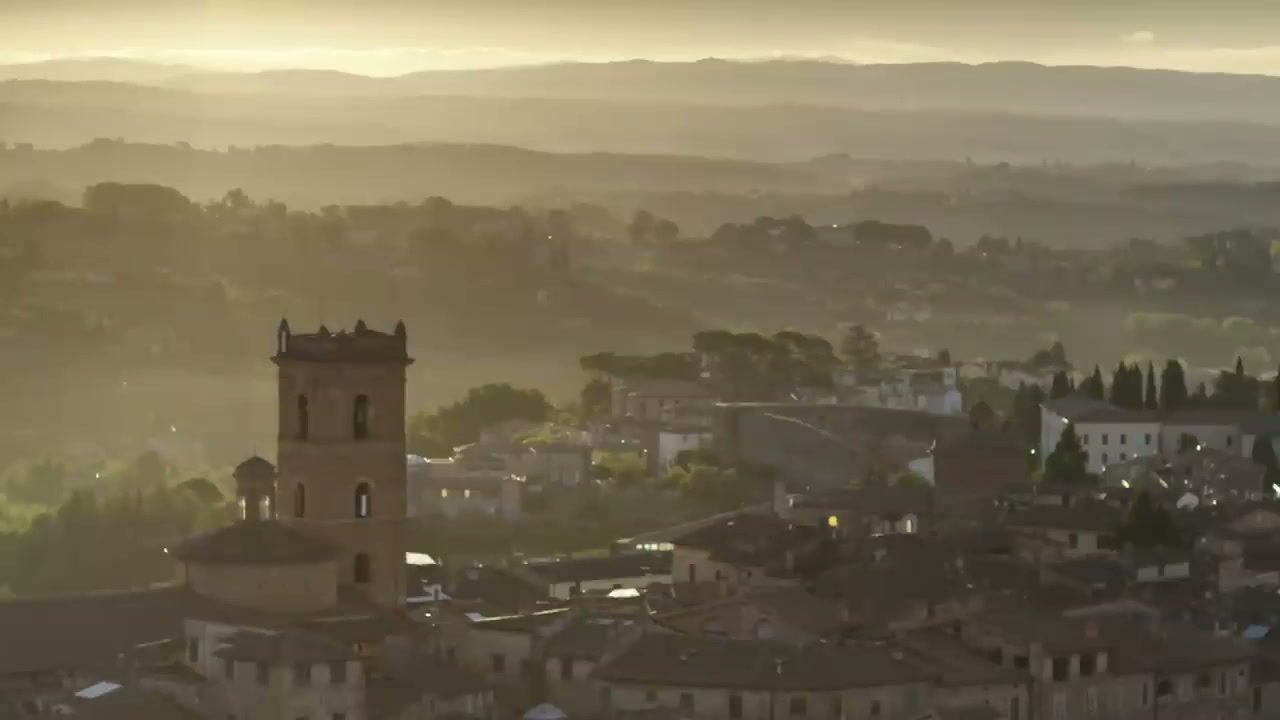 Siena's rooftops and a church tower against layered Tuscan hills in golden morning haze