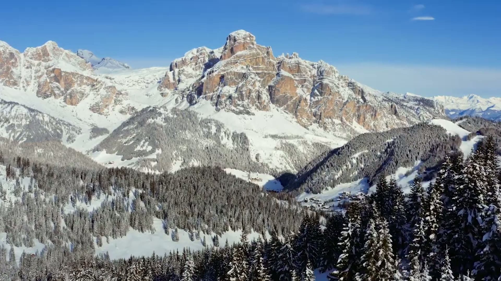 Cime innevate delle Dolomiti e pinete in Alta Badia sotto un cielo azzurro terso